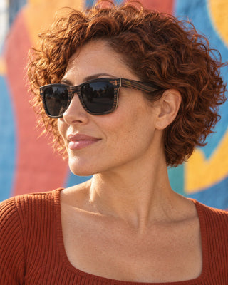 Barrio Logan polarized sunglasses worn by a woman in front of a colorful mural in Barrio Logan, San Diego