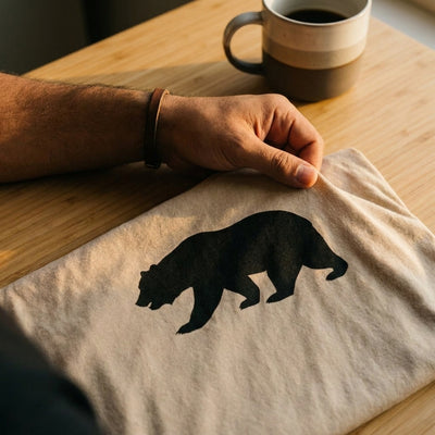 Close-up detail of the California Bear Tee fabric and solid black silhouette print, Bella+Canvas 3001 sand tan cotton, Cali Life Co.